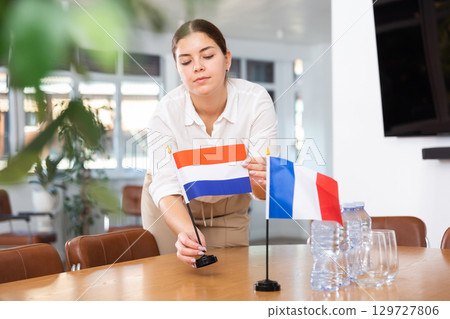 Employee of delegation prepares negotiating table - sets up flag of Netherlands and France 129727806