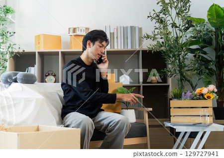 Communication. Young man on the phone while pointing at a floral arrangement in his workspace. 129727941
