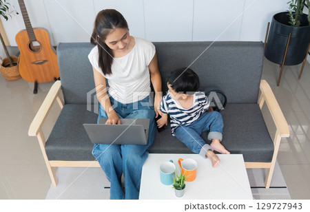 Mother multitasking with laptop while son engages nearby Mother multitasking with laptop while son engages nearby 129727943