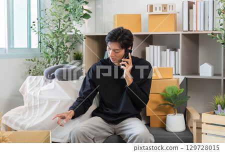 Remote Work. Young man engaged in a phone conversation while organizing his workspace. 129728015
