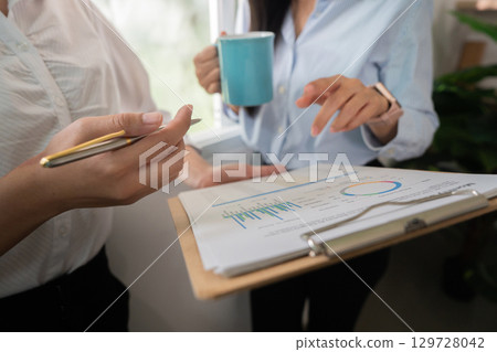 Data Review. Two women analyzing business metrics in a bright office environment. 129728042