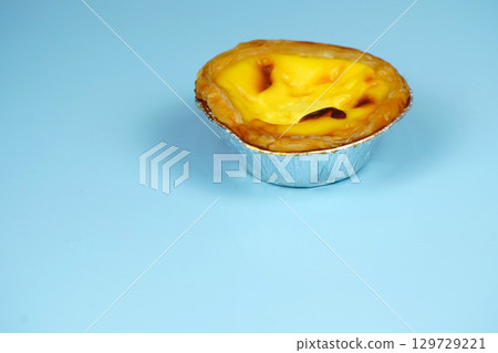 A delicious Portuguese egg tart with a flaky crust and creamy filling, sitting on a light blue background. A delicious Portuguese egg tart with a flaky crust and creamy filling, sitting on a light blue background. 129729221