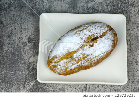 A small, freshly baked loaf of bread dusted with powdered sugar, sitting on a white rectangular plate. A small, freshly baked loaf of bread dusted with powdered sugar, sitting on a white rectangular plate. 129729235