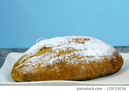 A small, freshly baked loaf of bread dusted with powdered sugar, sitting on a white rectangular plate. 129729236