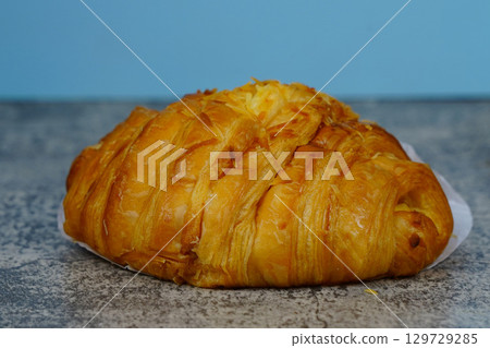 A fresh, flaky, and golden-brown croissant sits on a gray table, with a blue background. 129729285