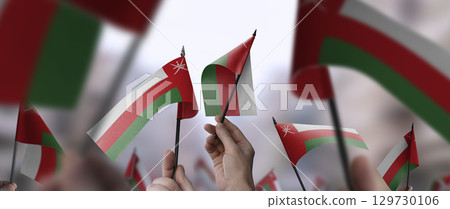 Oman flags in their hands on a blurred urban background 129730106