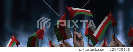 Oman flags in their hands on a blurred urban background 129730108