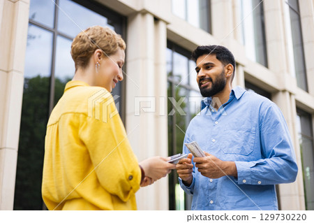 Two people exchanging money outdoors near a building. The man is holding cash, the woman is receiving it. Two people exchanging money outdoors near a building. The man is holding cash, the woman is receiving it. 129730220