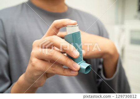 Asthma and chronic obstructive pulmonary disease COPD, Asian young man using metered dose inhaler MDI. 129730812