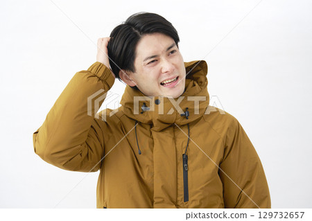 A man wearing a down jacket is worried on a white background A man wearing a down jacket is worried on a white background 129732657