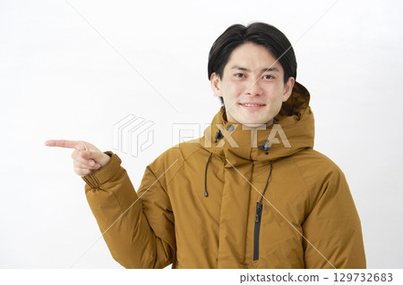 A man wearing a down jacket points to the left on a white background A man wearing a down jacket points to the left on a white background 129732683