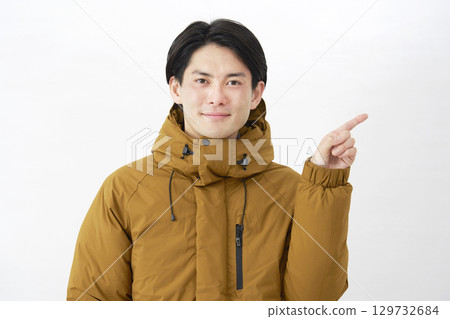 A man wearing a down jacket points to the right on a white background A man wearing a down jacket points to the right on a white background 129732684