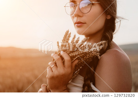 Woman wheat field. Agronomist, Woman farmer check golden ripe barley spikes in cultivated field. A woman is holding a bunch of wheat in her arms. 129732820