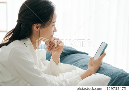 A woman in pajamas looking at her smartphone while sleeping 129733475