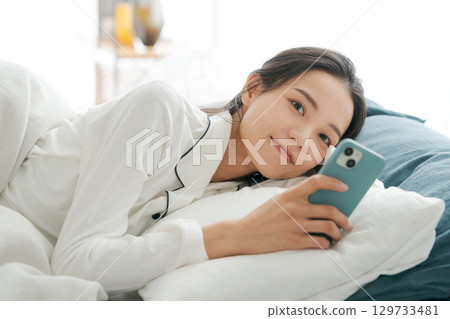 一位穿著睡衣的女士在睡覺時看著她的智慧型手機 一位穿著睡衣的女士在睡覺時看著她的智慧型手機 129733481