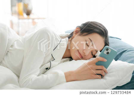 一位穿著睡衣的女士在睡覺時看著她的智慧型手機 129733484