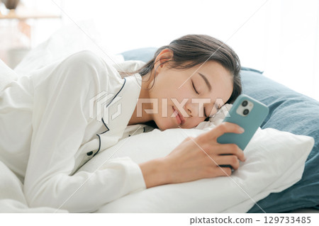一位穿著睡衣的女士在睡覺時看著她的智慧型手機 129733485