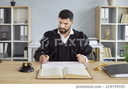 Portrait of male judge wearing judicial robe working in office having court verdict. Portrait of male judge wearing judicial robe working in office having court verdict. 129734505