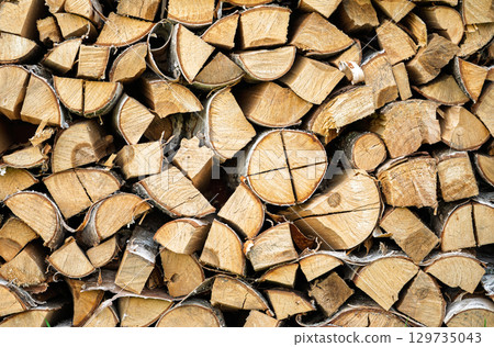 Firewood background, stack of chopped birch logs, natural wooden texture or pattern, preparation for winter heating season, sustainable energy and fuel theme 129735043