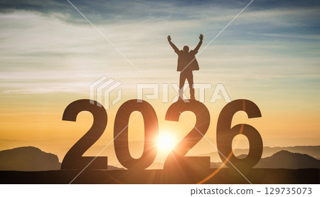 Silhouette of a successful person standing on 2026 number, celebrating with arms raised at sunrise, a concept of achievement Silhouette of a successful person standing on 2026 number, celebrating with arms raised at sunrise, a concept of achievement 129735073