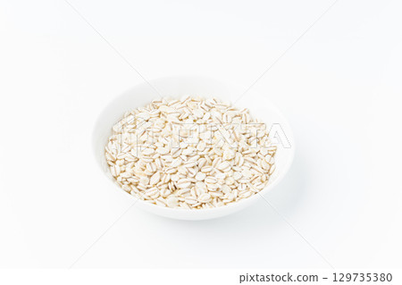 Rolled barley in a plate on a white background 129735380