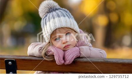 Thoughtful young caucasian girl in cozy winter attire resting on park bench in autumn. 129735712