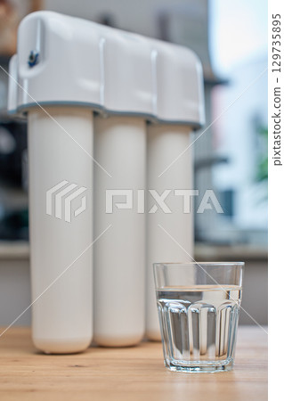 Glass of filtered drinking water and water filtration system on kitchen table Glass of filtered drinking water and water filtration system on kitchen table 129735895