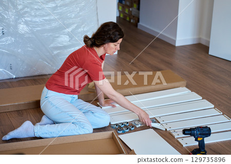 Woman assembling furniture at home with tools and parts Woman assembling furniture at home with tools and parts 129735896