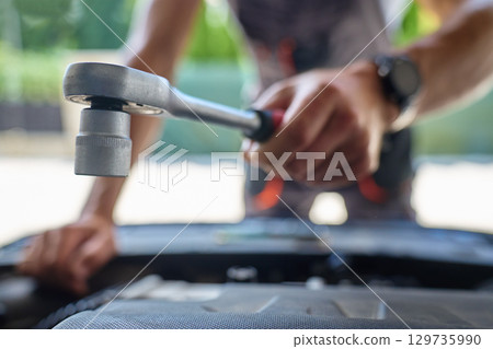 Mechanic holding wrench over car engine during repair 129735990