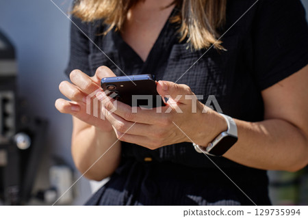 Close up of woman holding smartphone in hand outdoors 129735994