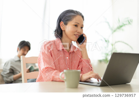 A woman looking at a computer while on the phone 129736957