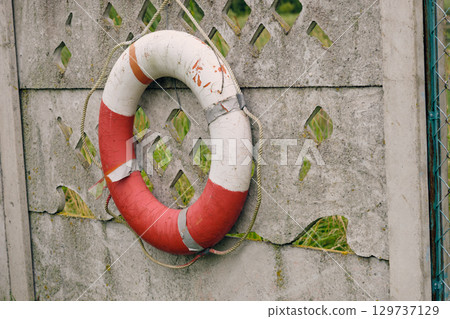 Lifebuoy hangs on a stone fence in a tranquil outdoor setting during overcast weather Lifebuoy hangs on a stone fence in a tranquil outdoor setting during overcast weather 129737129