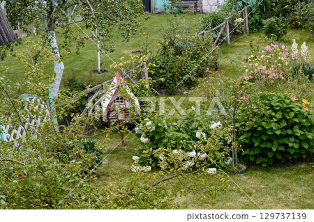 Colorful garden with flowers, greenery, and a decorative playhouse in a serene outdoor setting during daylight 129737139
