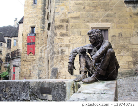 Sarlat-la-Caneda, France - October 10, 2016 - Bronze statue of Le Badaud, The Onlooker, a seated young man Sarlat-la-Caneda, France - October 10, 2016 - Bronze statue of Le Badaud, The Onlooker, a seated young man 129740752