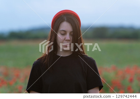 Young Woman in Poppy Field with Red Hat 129742444