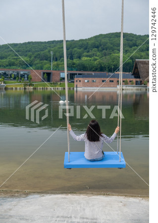 Person Relaxing on Swing by Scenic Lake 129742446