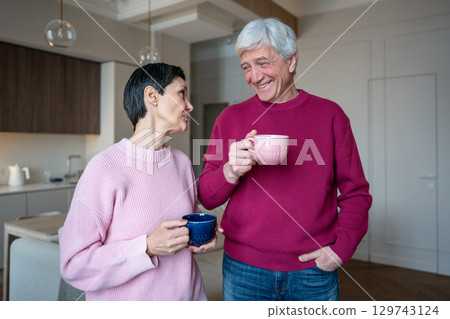 Elderly man laughing at wife work story. Couple drinking tea together after workday at home Elderly man laughing at wife work story. Couple drinking tea together after workday at home 129743124
