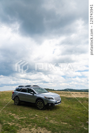 Silver SUV on Grassy Hill with Cloudy Sky Silver SUV on Grassy Hill with Cloudy Sky 129743941