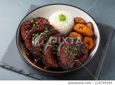 Venezuelan asado negro slow cooked beef in a dark sauce with rice and fried plantains 129744394