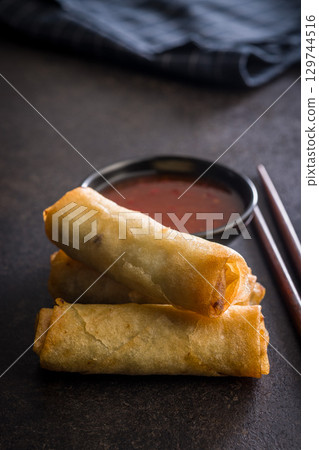 Fried spring rolls and sweet and sour sauce on wooden table. 129744516