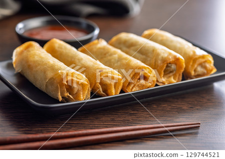 Fried spring rolls and sweet and sour sauce on wooden table. 129744521