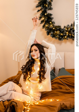 Woman Relaxing with Holiday Lights on Bed 129745859