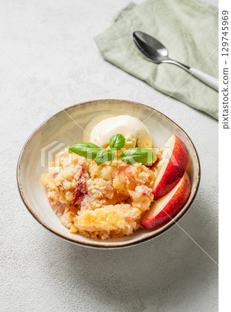 Peach crumble or cobbler with vanilla ice cream scoops and cinnamon on a plate on a light background Peach crumble or cobbler with vanilla ice cream scoops and cinnamon on a plate on a light background 129745969