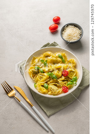 Tortellini pasta with parmesan, pesto and basil in a plate on a light background with tomato Tortellini pasta with parmesan, pesto and basil in a plate on a light background with tomato 129745970