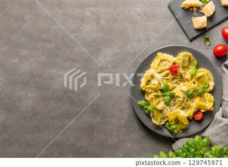 Tortellini pasta with parmesan, pesto and basil in a plate on a dark background with cheese 129745971