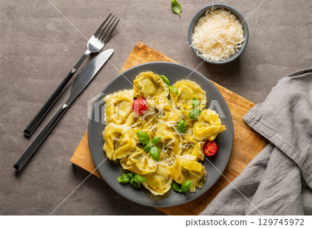 Tortellini pasta with parmesan, pesto and basil in a plate on a wooden board on a dark background 129745972