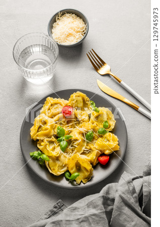Tortellini pasta with parmesan, pesto and basil in a plate on a light background with glass of water 129745973
