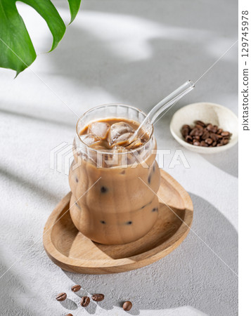 Ice latte coffee in a glass with milk and straw on a wooden plate on light background 129745978