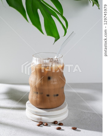 Ice latte coffee in a glass with milk and straw on a light background with coffee beans, monstera Ice latte coffee in a glass with milk and straw on a light background with coffee beans, monstera 129745979