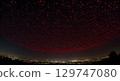 Red light drone swarm over cityscape at night with dark sky and glowing lights 129747080